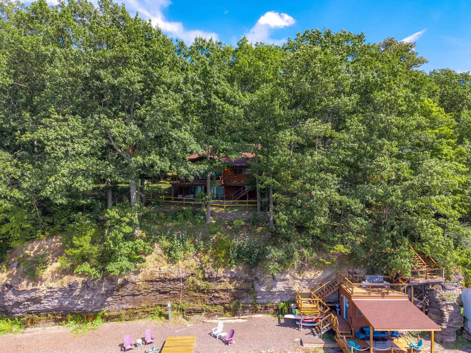 The property in context from the water — main house on the bluff, deck level below, boathouse at the shale beach