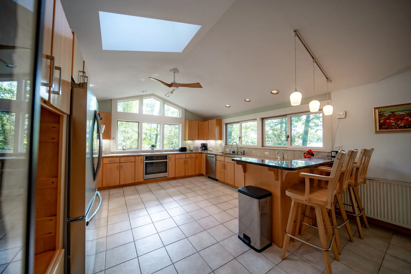 Kitchen at Lakeside Landing FLX — vaulted ceiling with skylight, wood cabinets, granite peninsula with barstools, lake-facing windows
