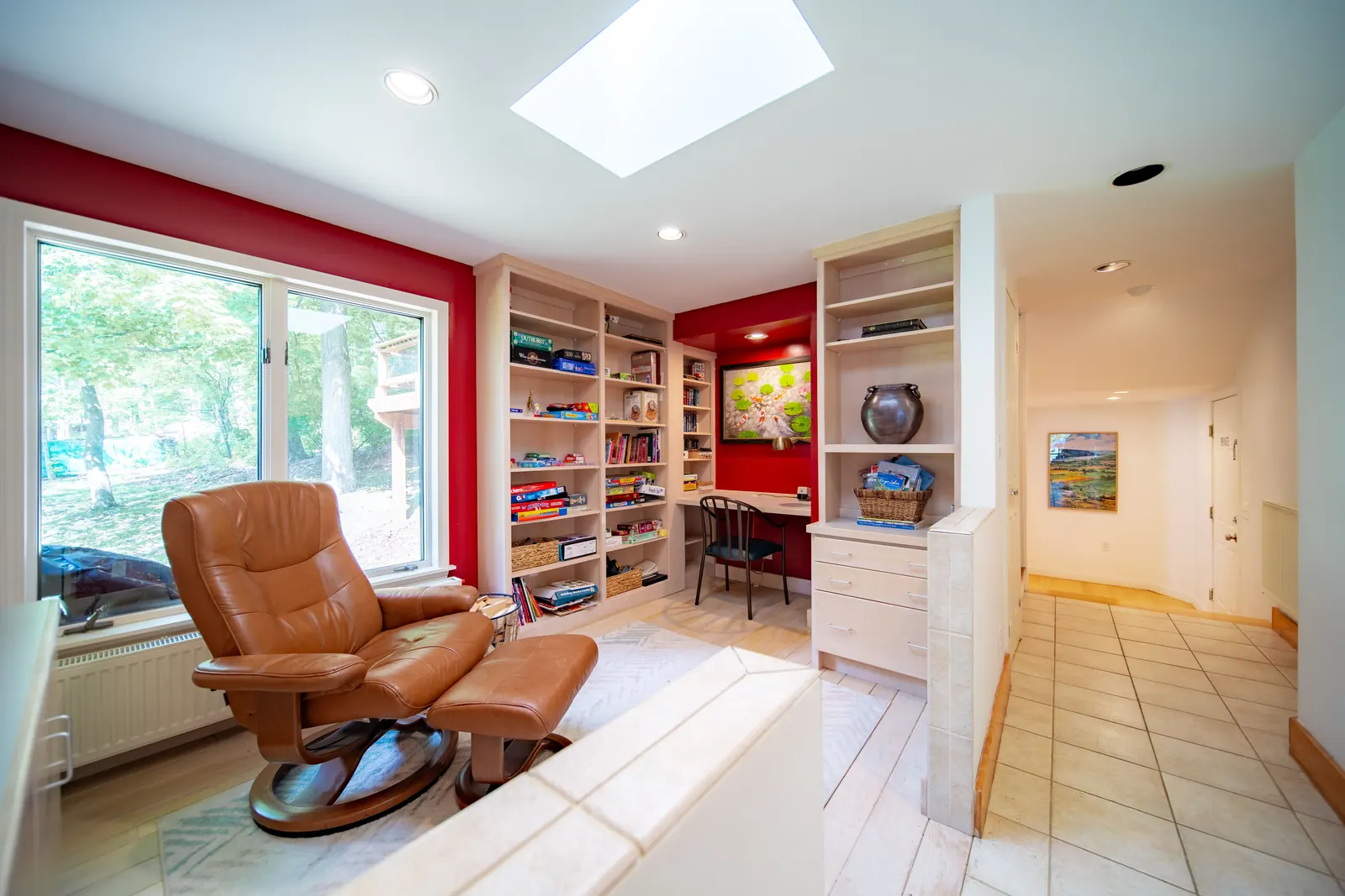 The games room at Lakeside Landing FLX — built-in shelves loaded with board games and books, leather recliner, skylight, red accent wall