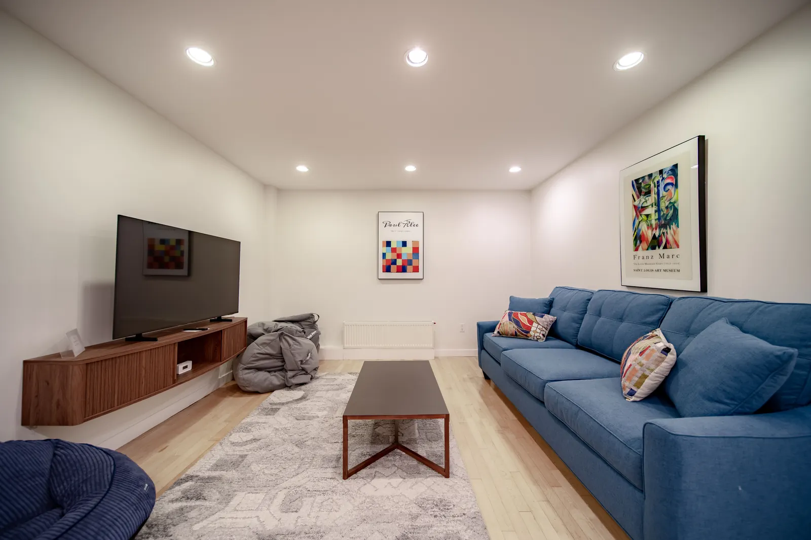 The TV room at Lakeside Landing FLX — blue sectional and hardwood floors, framed prints, quiet family space