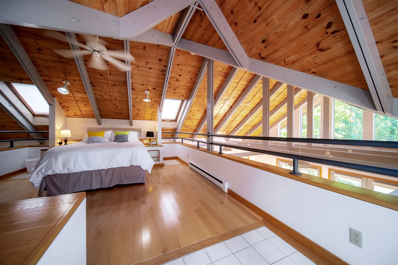 The loft bedroom at Lakeside Landing FLX — vaulted knotty-pine ceiling with exposed beams, skylights, king bed and a wall of tall windows over the lake