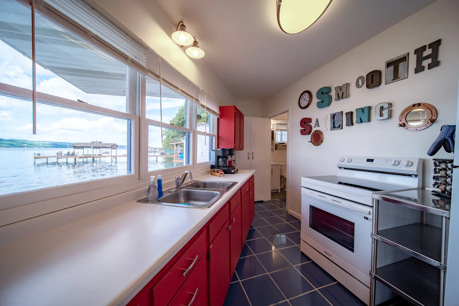 The Smooth Sailing FLX galley kitchen — red cabinets, marquee letters, lake view over the sink, cottage feel